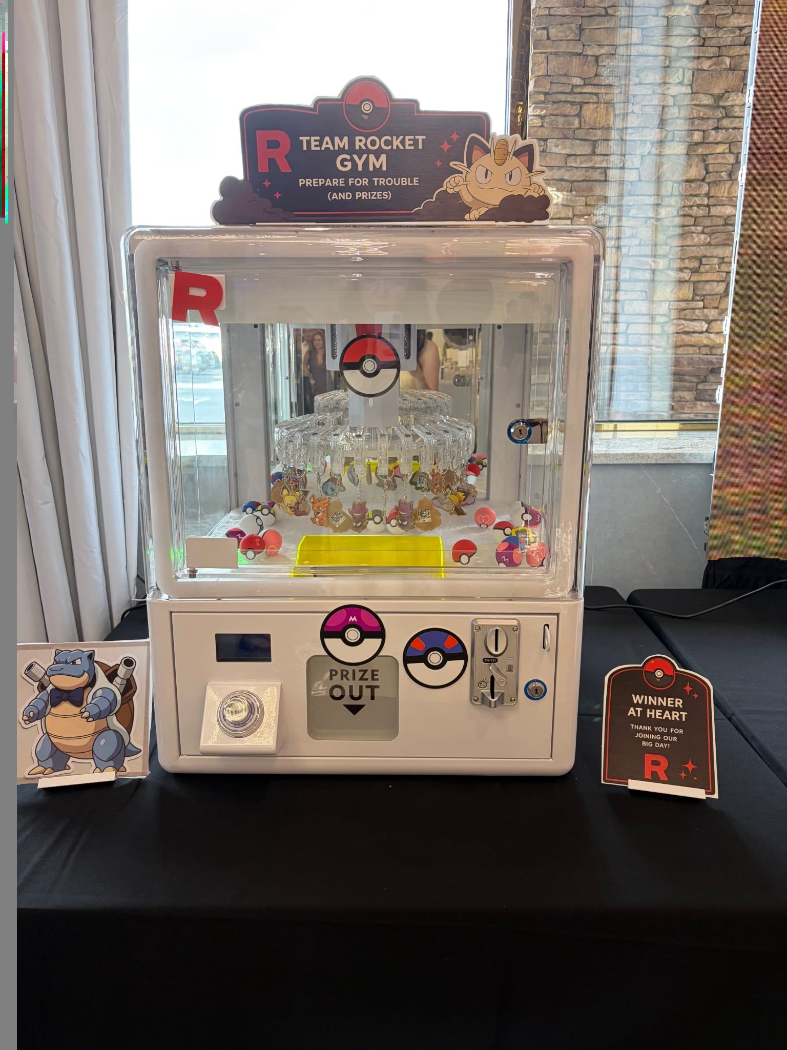 Claw machine with a custom dark 'Team Rocket Gym' topper sign filled with keychain prizes